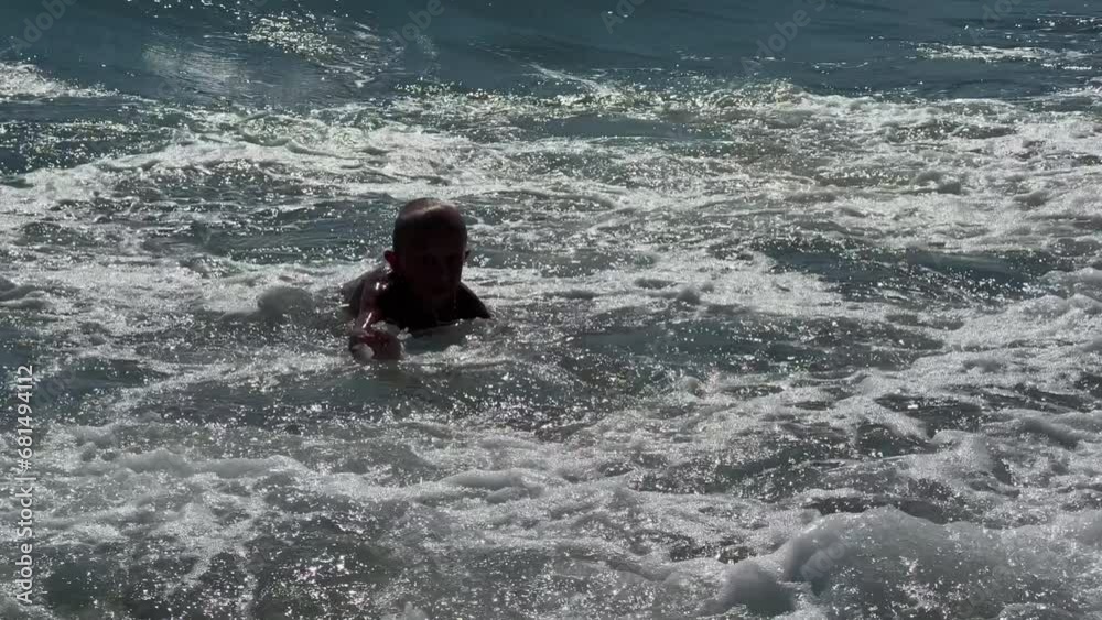 A happy child with a swimming circle swims on the sea on a sunny day. The boy has fun on the waves, moves his feet in the water, splashes, hitting the waves. Black Sea. 4K A happy child with a swimming circle swims on the sea on a sunny day. The boy has fun on the waves, moves his feet in the water, splashes, hitting the waves. Black Sea. 4K