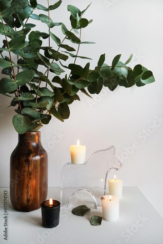 Eucalyptus branches in a wooden vase next to candles on a light background