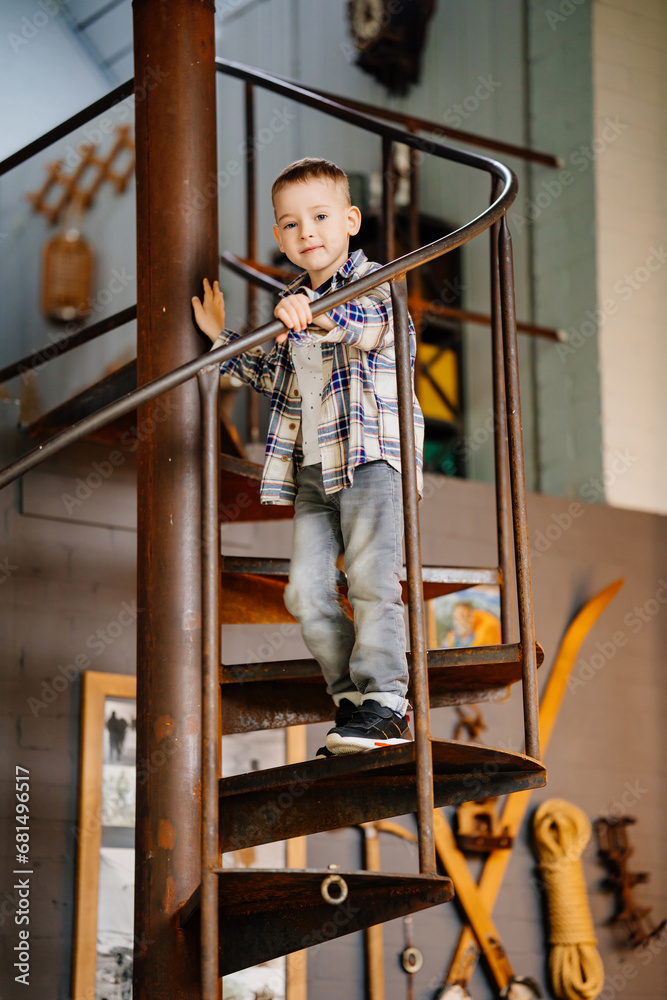 Obraz premium Funny little boy in plaid shirt and jeans in the interior of a country house. 