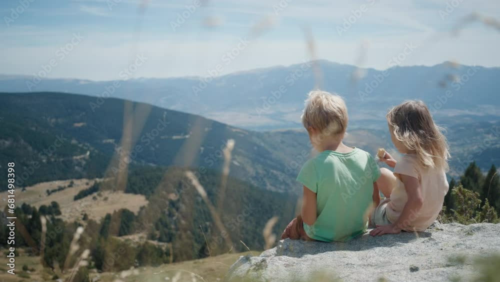 Brother and sister sit and eat snack on mountain hill during hiking on vacation