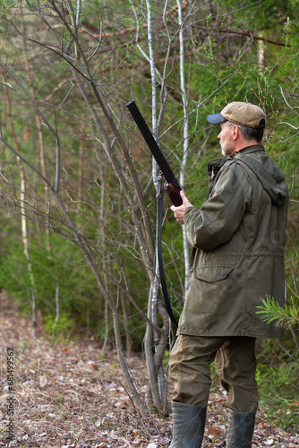 a hunter stands with a gun in his hands in a forest clearing