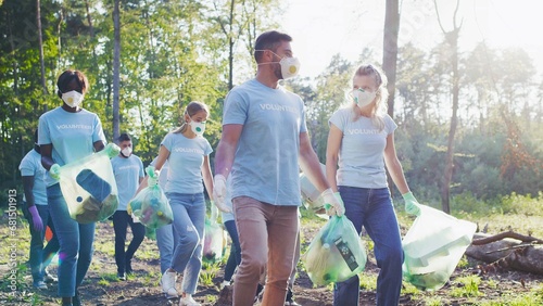 Multiracial, diverse group of volunteers collecting garbage, waste. Active environmentalists wearing protective masks walking together, chatting with each other. Volunteering, global concern concept