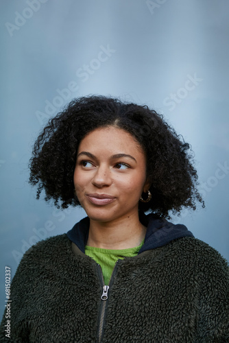 Portrait of a biracial girl with curly hair standing against blue wall.Concept of gen z, fashion and self expression.