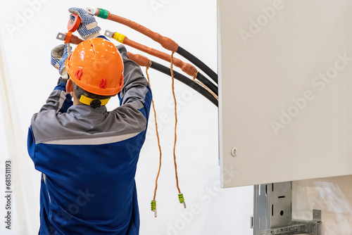 Man installer insulates high-voltage cable. Guy prepares wires to supply electricity. Electrician wraps insulating tape at cable. Electrical engineer with back to camera. Man doing electrical work photo