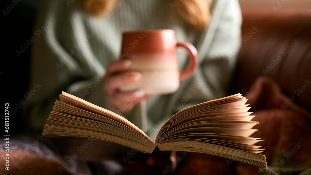 Close Up Of Woman At Home In Winter Jumper With Warming Hot Drink In Mug Reading Book - obrazy, fototapety, plakaty 