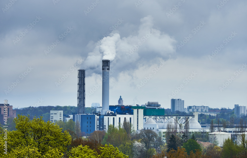 Tall smoking chimney with a cloud of smoke surrounded by the city shows how pollution is part of our day to day life. Smokestack in a factory polluting the air by people 's houses. Spandau, Germany