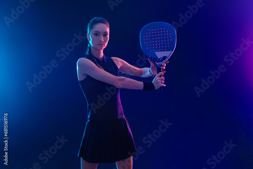 Padel tennis player with racket on tournament. Girl athlete with paddle racket on court with neon colors. Sport concept. Download a high quality photo for design of a sports app or tour events. © Mike Orlov