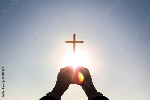 Brightly shining sunlight and silhouette of Christian hands holding high the cross of Jesus Christ symbolizing death and resurrection
 photo