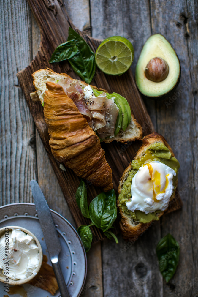 Croissant sandwiches with jamon ham serrano paleta iberica, avocado, basil, egg pashot on blue background. Delicious snack, appetizers, tapas. Croissant sandwiches with jamon ham serrano paleta iberica, avocado, basil, egg pashot on blue background. Delicious snack, appetizers, tapas.
