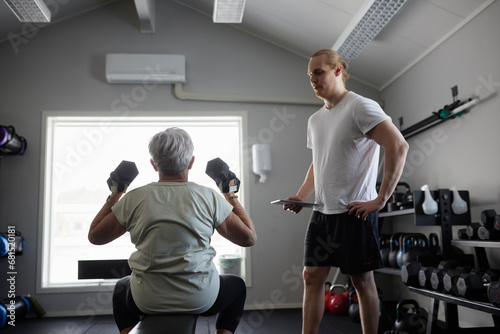 Woman exercising with dumbbell with trainer checking his progress