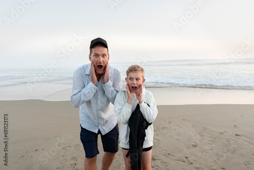 Father and son standing on sandy be ach and making faces photo