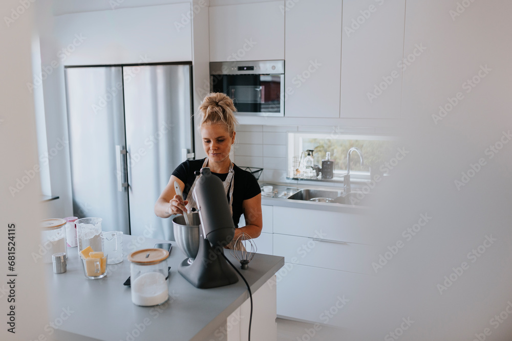 Young woman using stand mixer in kitchen