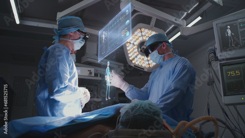 Doctors perform surgery in hospital operating room wearing AR headsets. 3D graphics of virtual AI holographic display showing vital signs and patient condition. VFX animation. Modern medicine concept. photo