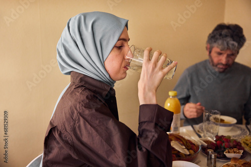 Woman in headscarf drinking water at dinner