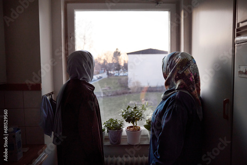Thoughtful women in headscarves looking through window photo