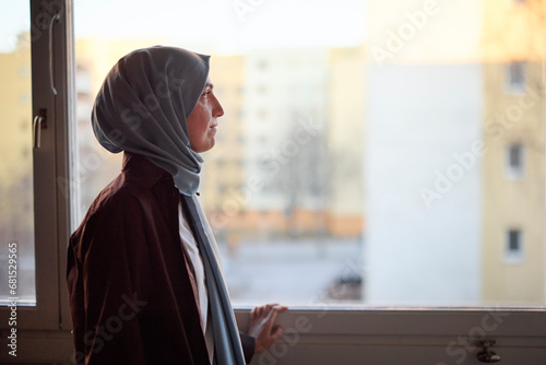 Thoughtful woman in headscarf looking through window photo