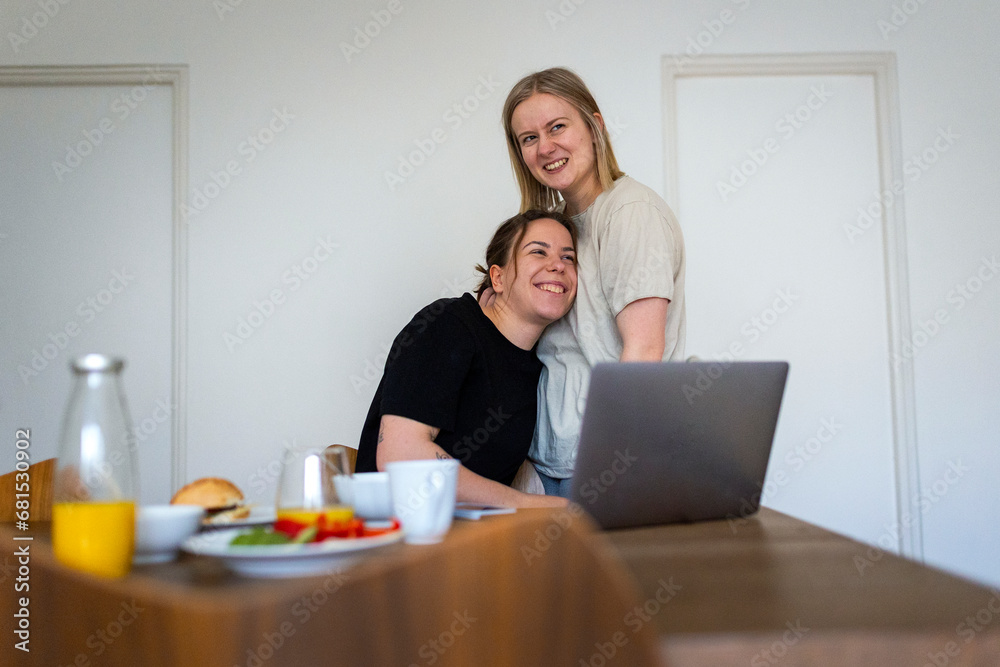 Happy affectionate lesbians embracing near dining table Happy affectionate lesbians embracing near dining table