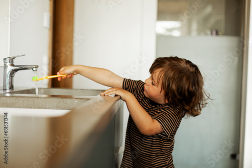 Boy holding toothbrush under running water from faucet