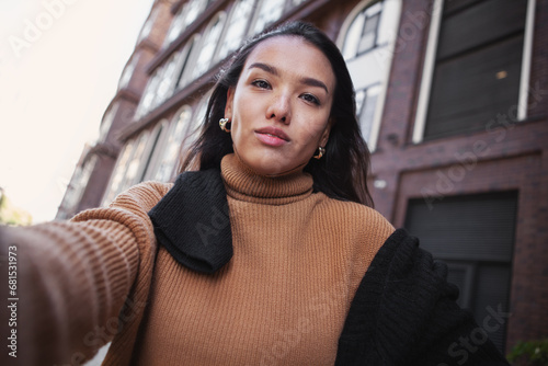 Candid Self portrait of brunette woman looking at camera outdoors. Beautiful female fashion model on street of city takes selfie photo