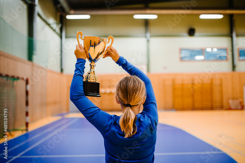 Rear view of girl holding golden trophy while standing in sports court photo
