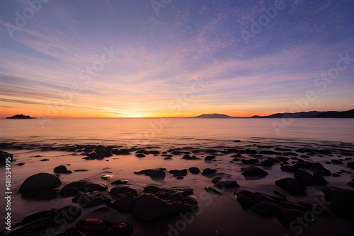 夕日が沈む夕焼けのビーチの岩場の美しい風景、水と砂に夕日が反射して輝いている
