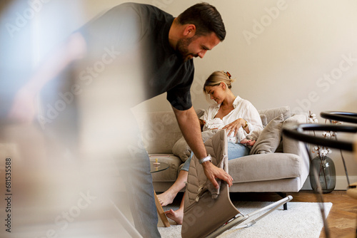 Father cleaning living room while mother breastfeeding son at home photo
