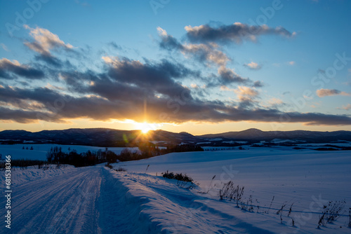 冬の夕暮れの道路と山陰に沈む太陽 