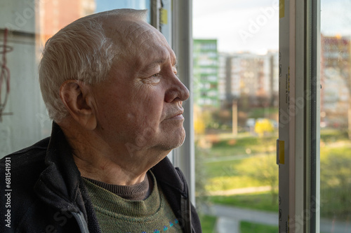 Portrait of a sad elderly man looking out the window at home. Lonely elderly man looking out the window