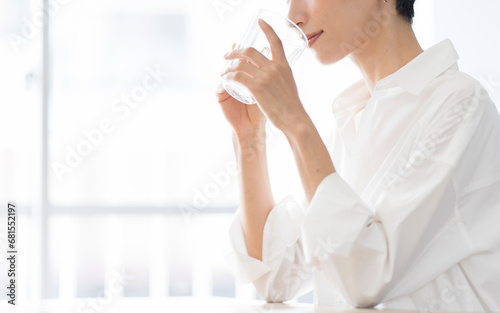 グラスに入った飲み物を飲む女性/白いシャツを着たミドル世代の日本人女性