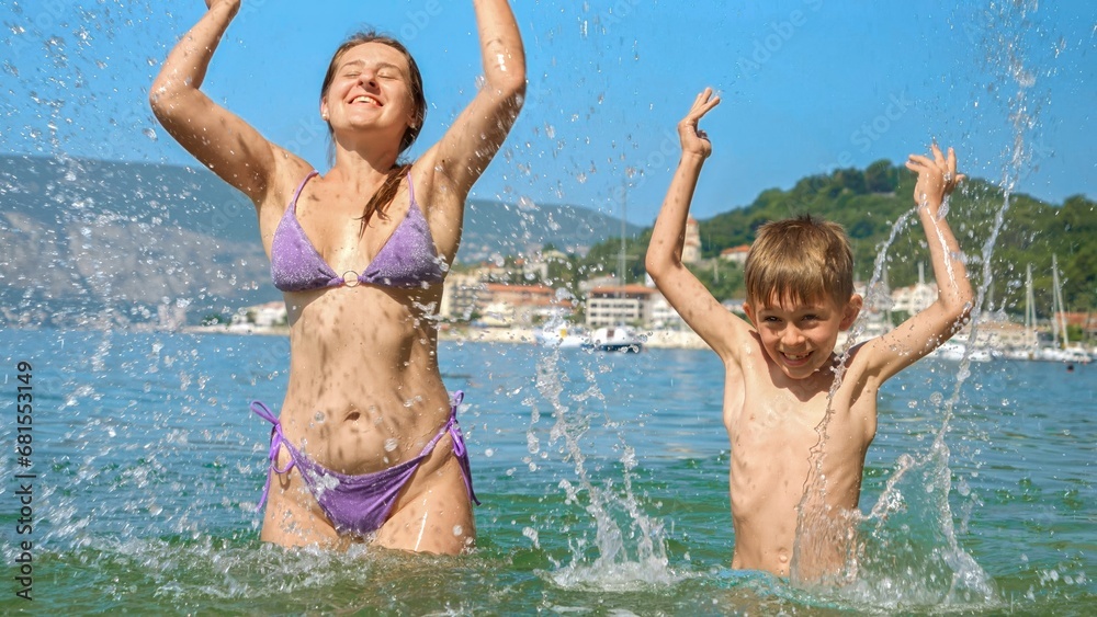 Happy cheerful excited boy splashing water with mother while relaxing on sunny sea beach Happy cheerful excited boy splashing water with mother while relaxing on sunny sea beach