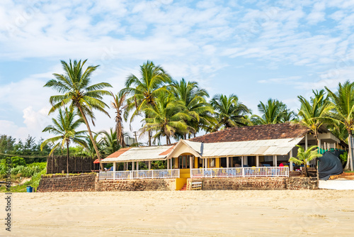 coconut trees on ocean coast near tropical shack or open cafe on beach with sunbeds © hiv360