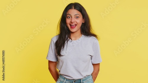 Funny comical playful Indian young woman making silly facial expressions grimacing fooling around, showing tongue, idiotic expression. Comedian Arabian girl on yellow background. People lifestyles photo