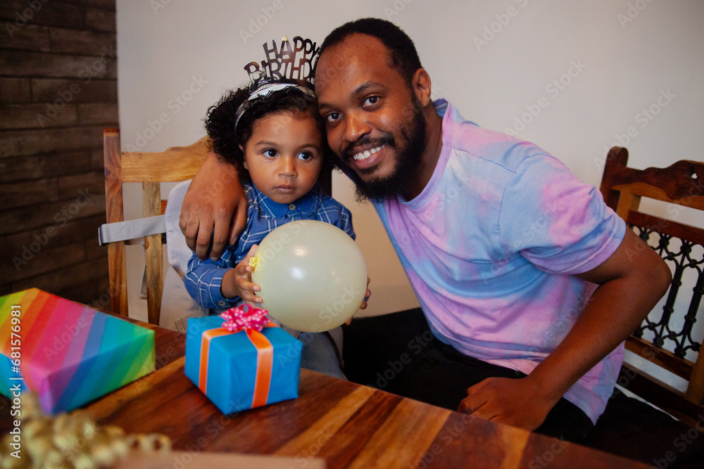 Fototapeta premium Young African father with biracial son celebrating his birthday and smiling into camera