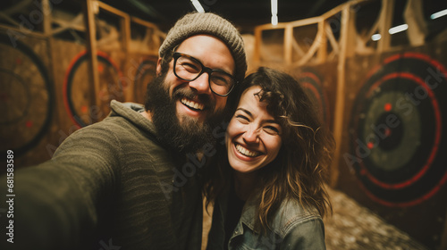 Smiling hipster couple taking a selfie in an axe-throwing or dart bar
