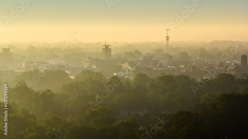 Hazy yellow sunrise with smog over city and green summer trees in Muncie, Indiana