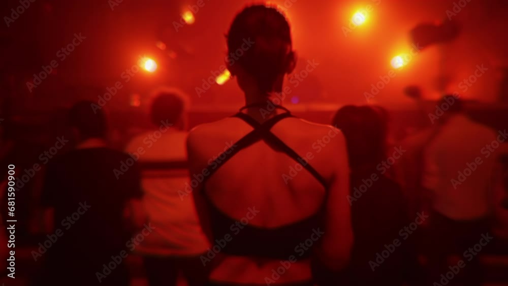 Girl dancing at nightclub party in red light, back view. People jumping at rave in underground techno club. Nightlife, modern music event and entertainment concept. Slow motion