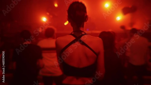 Girl dancing at nightclub party in red light, back view. People jumping at rave in underground techno club. Nightlife, modern music event and entertainment concept. Slow motion
