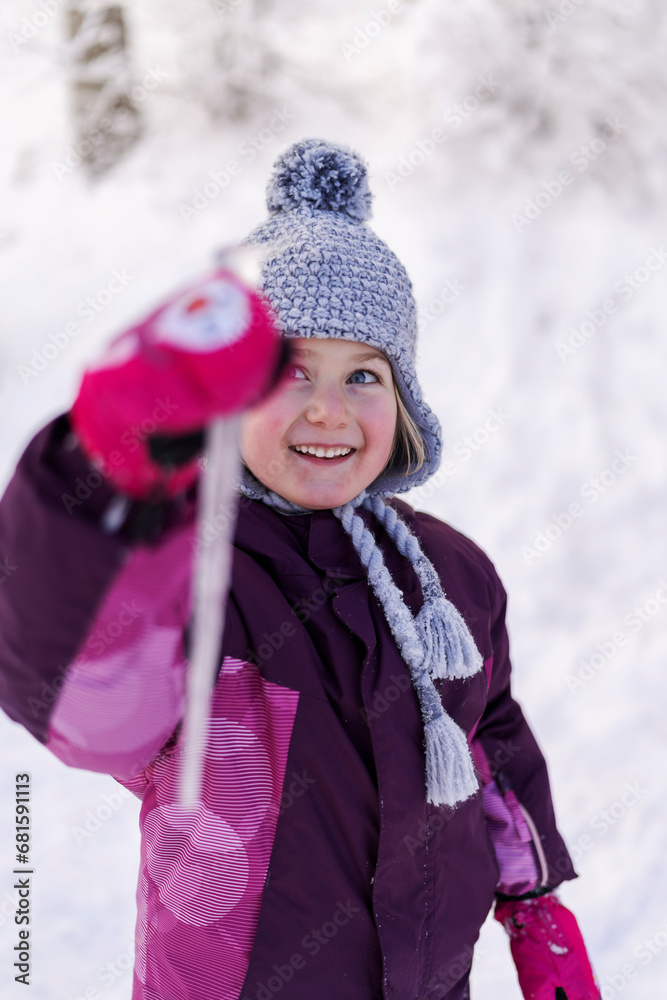 A smiling girl in winter attire holds a icicles, with a backdrop of snowy trees, radiating winter fun A smiling girl in winter attire holds a icicles, with a backdrop of snowy trees, radiating winter fun