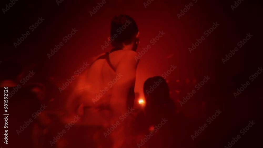 Girl dancing at rave party in techno club in crowd at electronic music festival. Young woman enjoying nightlife on nightclub dance floor with flashing red lights