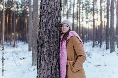 Attractive brunette female nature lover hugging tree at pine forest during the winter time.