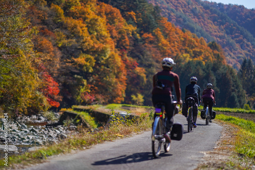 A group of cyclist enjoying riding by the river with beautiful scenery of autumn leaves in Kaida Kogen, Nagano Prefecture, Japan. (Selective focus on second cyclist)