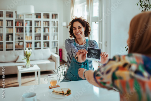 Excited Woman Showing Ultrasound to Friend Over Lunch photo