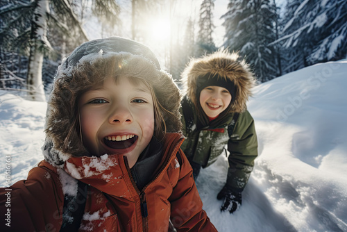 dos niños haciéndose un selfie en un bosque nevado, vestidos con ropa de invierno