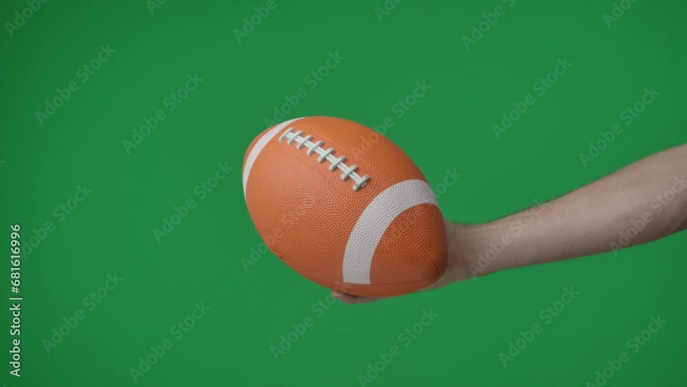In a shot on a green background, chromakey male hand that holds, holds out an oval shaped ball for American soccer, it is inflated, bright color. This could be a place for your advertisement. In a shot on a green background, chromakey male hand that holds, holds out an oval shaped ball for American soccer, it is inflated, bright color. This could be a place for your advertisement.