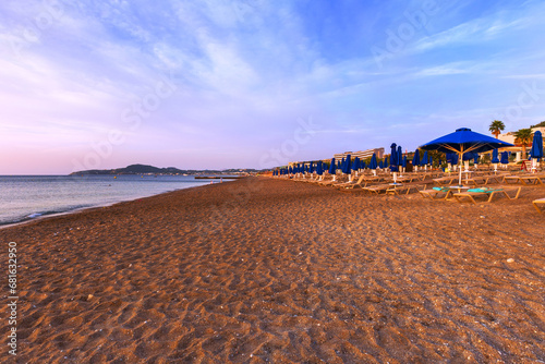 Pebble beach with sunbeds and blue umbrellas near Faliraki on the island of Rhodes.