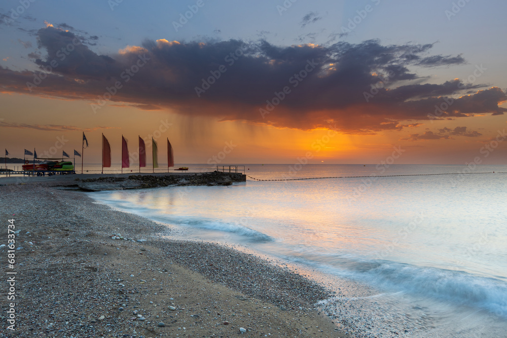 Rhodes island pebble beach, pier with flags and beautiful sunrise with dramatic sky with clouds.