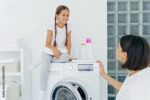 Mother and daughter enjoy laundry time together in a bright white room