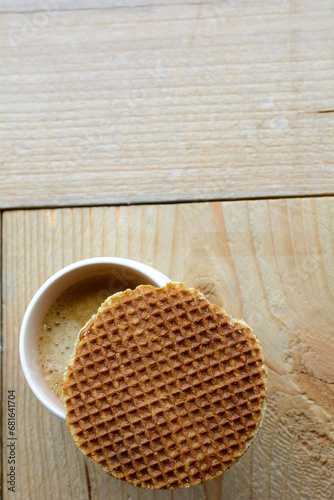 One stroopwafel with one white cup of black coffee on the wooden background. A cup of coffee on the wooden table with a biscuit