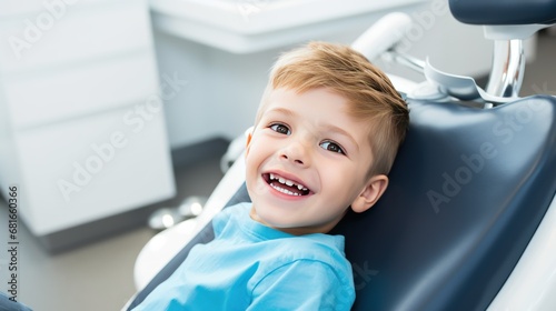 Photo of a smiling happy little Caucasian boy sitting in a chair in a dental office. He is waiting for the dentist for an oral procedure. photo