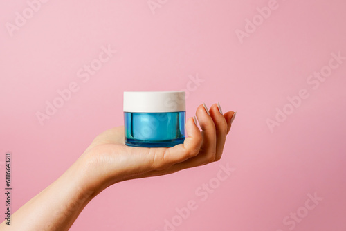 Elegant female hand holding blue glass jar of cosmetic cream on pink background. copy space